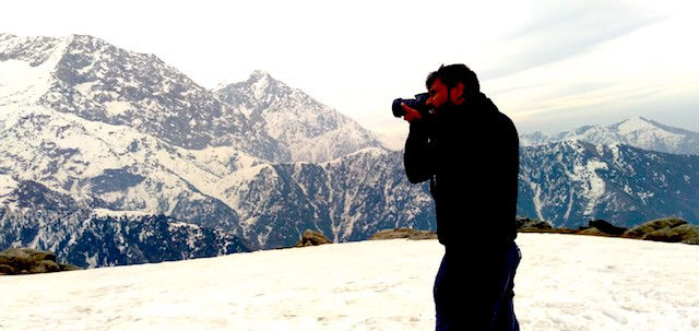 a hiker taking a photograph of the dhauladhar range from triund 